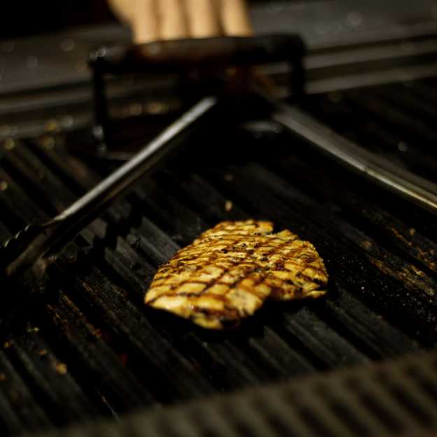 A Lone grilled chicken on a grill with tongs.