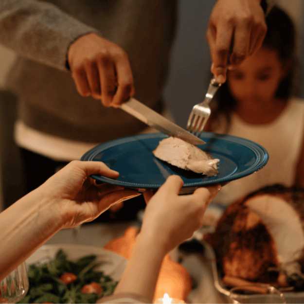 Someone serving turkey to a person holding a blue plate up.