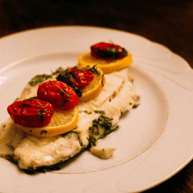 Cooked fish displayed with lemons and cherry tomatoes on a white plate.