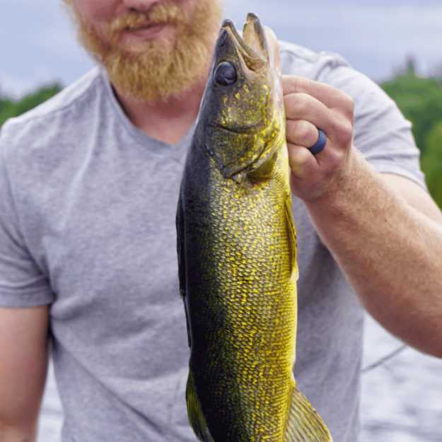 A Blonde haired man holding up a walleye.