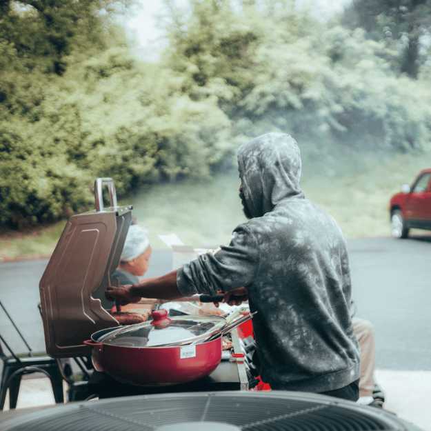 A Colored man moving hotdogs at a barbeque.