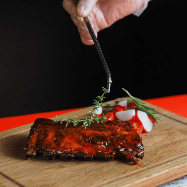 Ribs covered in sauce on a cutting board next to cut up radish and garnished.