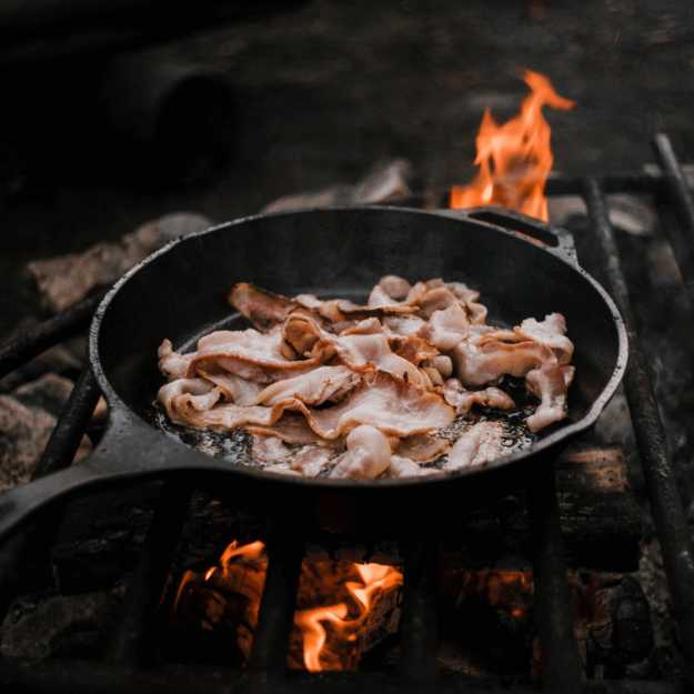 Bacon being cooked on a iron cast pan.