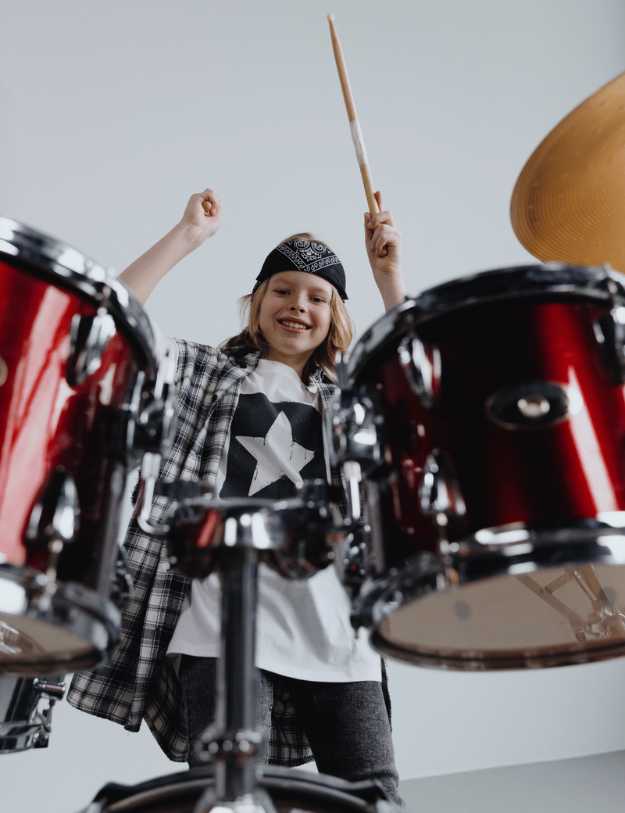 A kid behind a drum set standing.