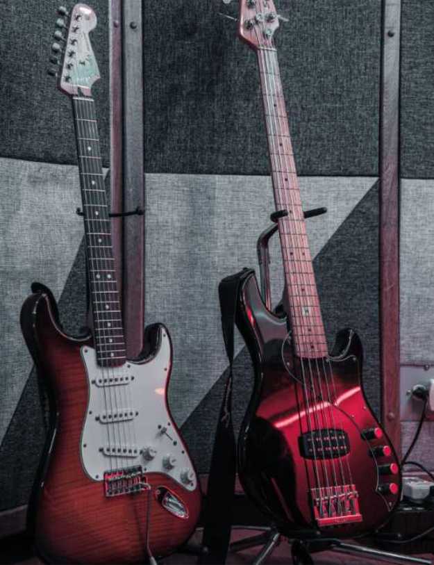 Two red guitars on their stands next to a wall.