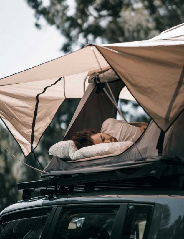 Man sleeping in a tent on the top of his car.