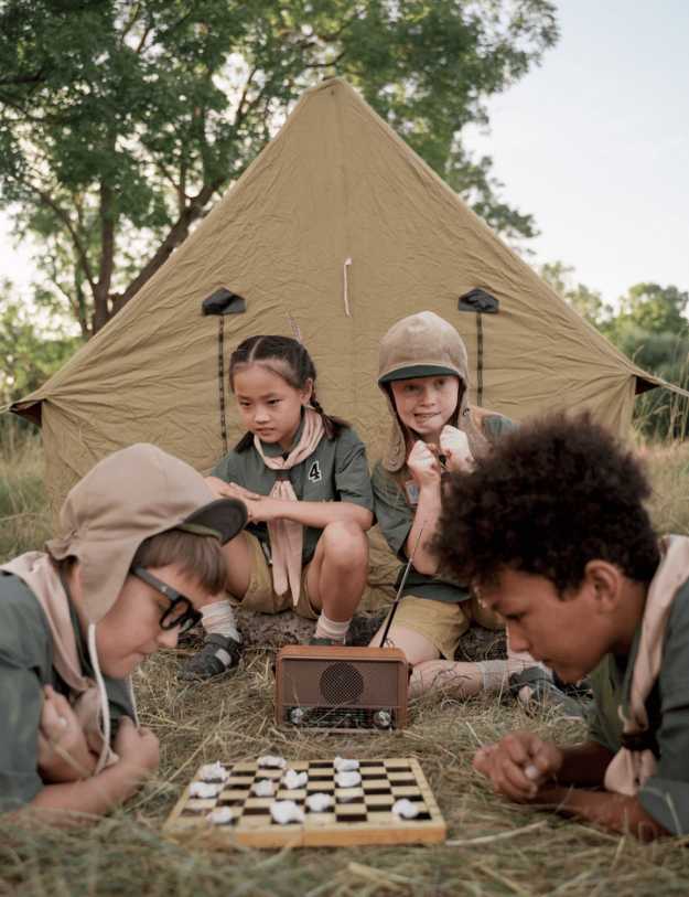 A bunch of kids playing chess next to a tent.