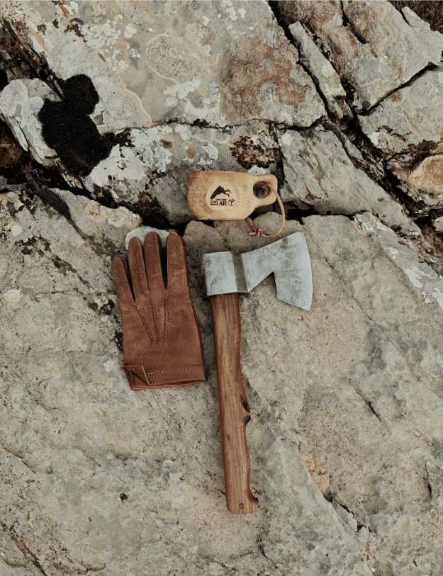 A glove, hatchet and its cover sitting on a rock.