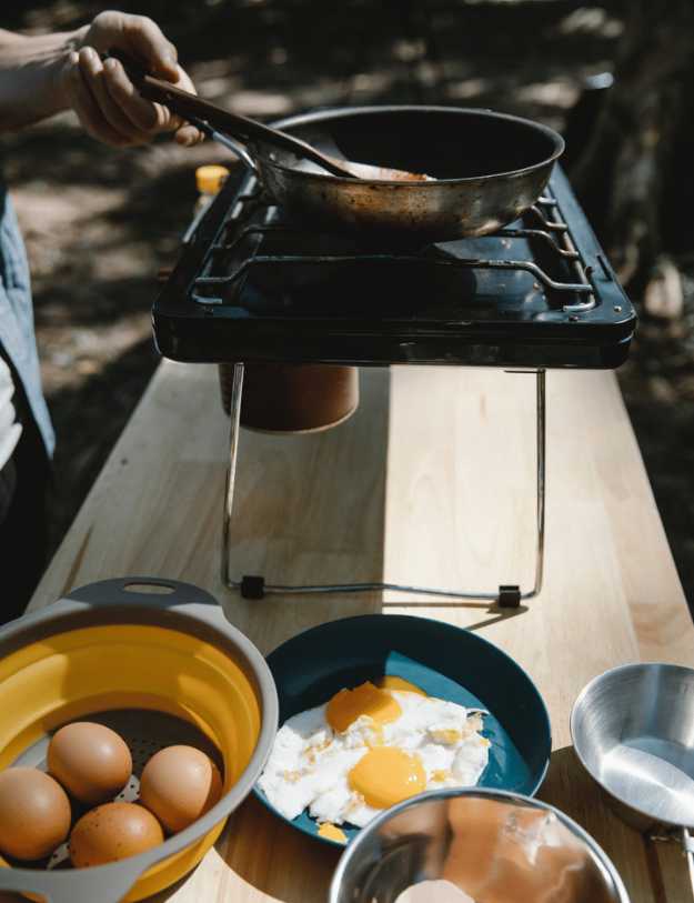 Someone cooking eggs on a table top camping kitchen.