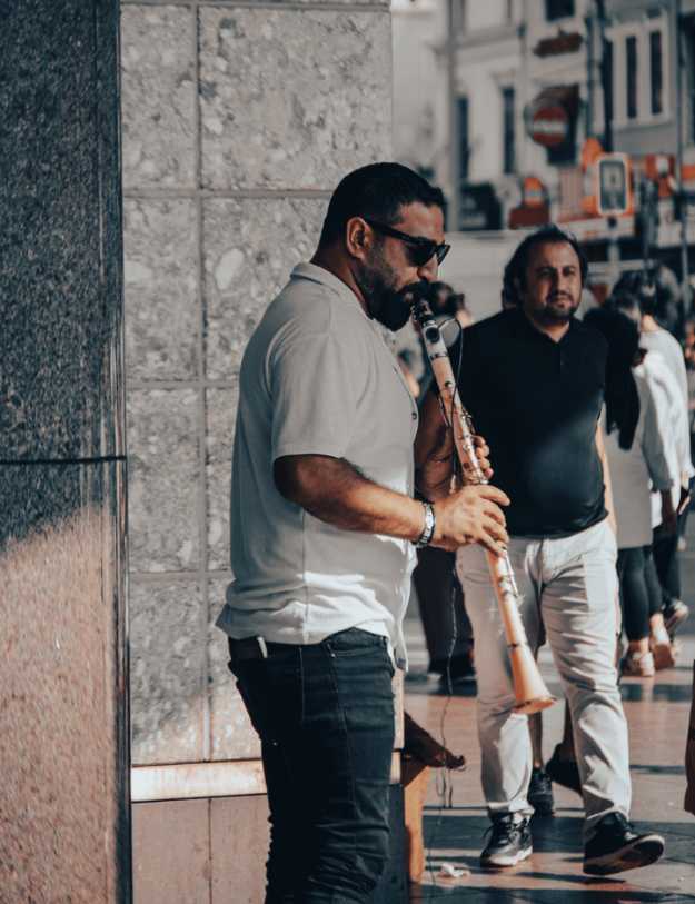 Man playing a clarinet on the sidewalk corner.