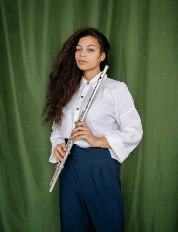 Colored woman holding a flute, posing in front of a green sheet.