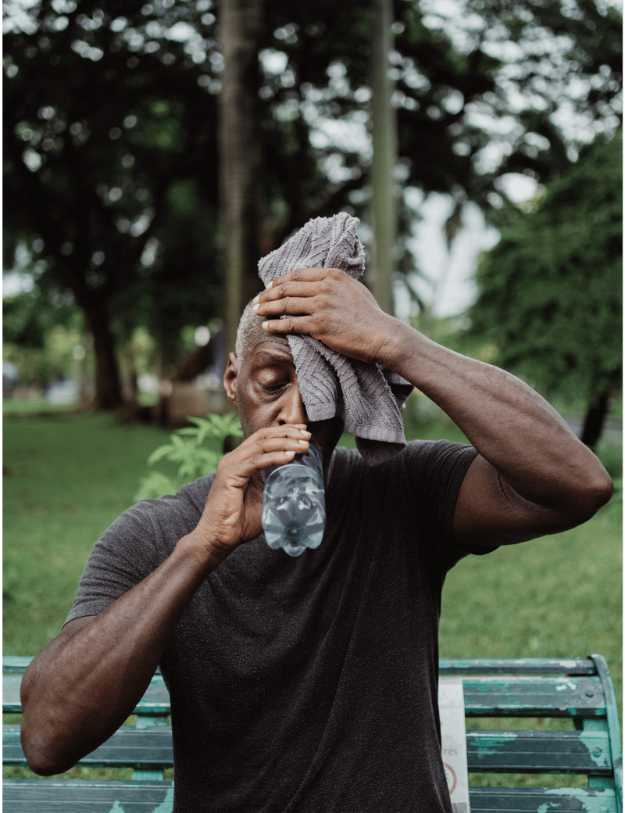 A colored older man wiping his forehead with a towel and drinking water. 