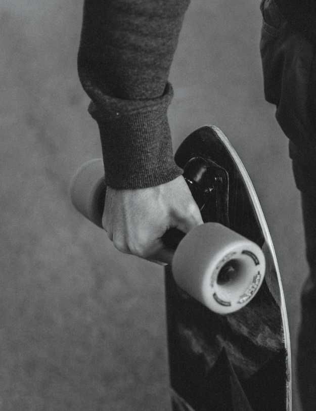 Black and white image of someone holding a skateboard by the axis.