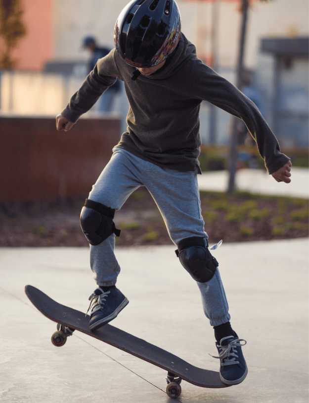 A Kid trying to do a flip with the skateboard in full protection