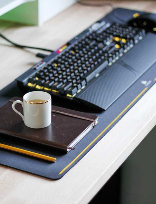 A work desk with a keyboard and a cup of coffee on a journal.