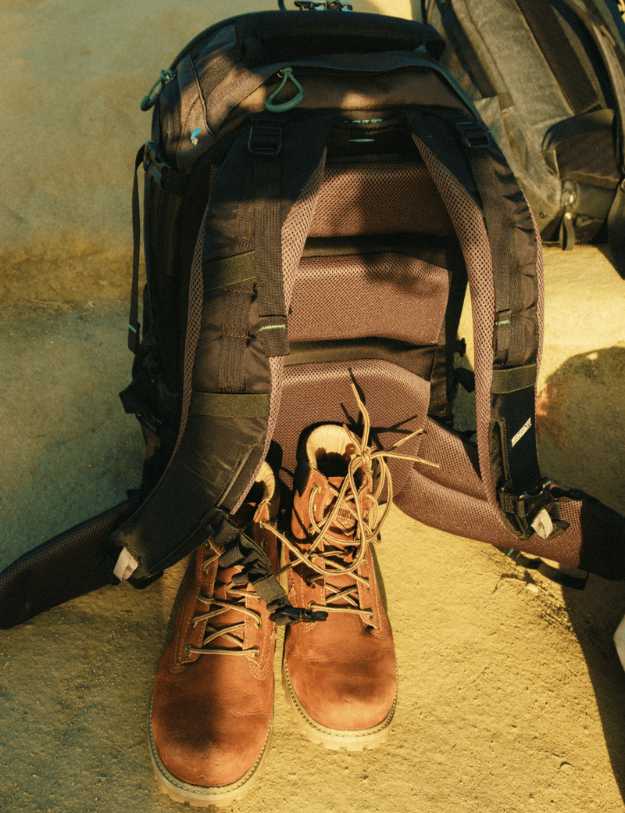 A pair of boots with a backpack on a dirt floor.