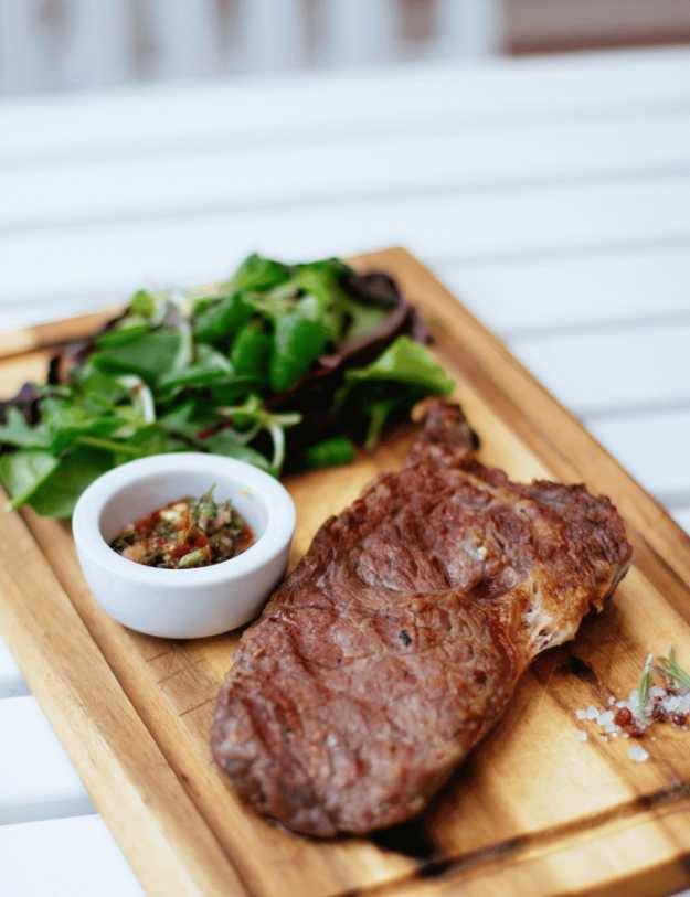 A steak on a cutting board with salsa and greens.