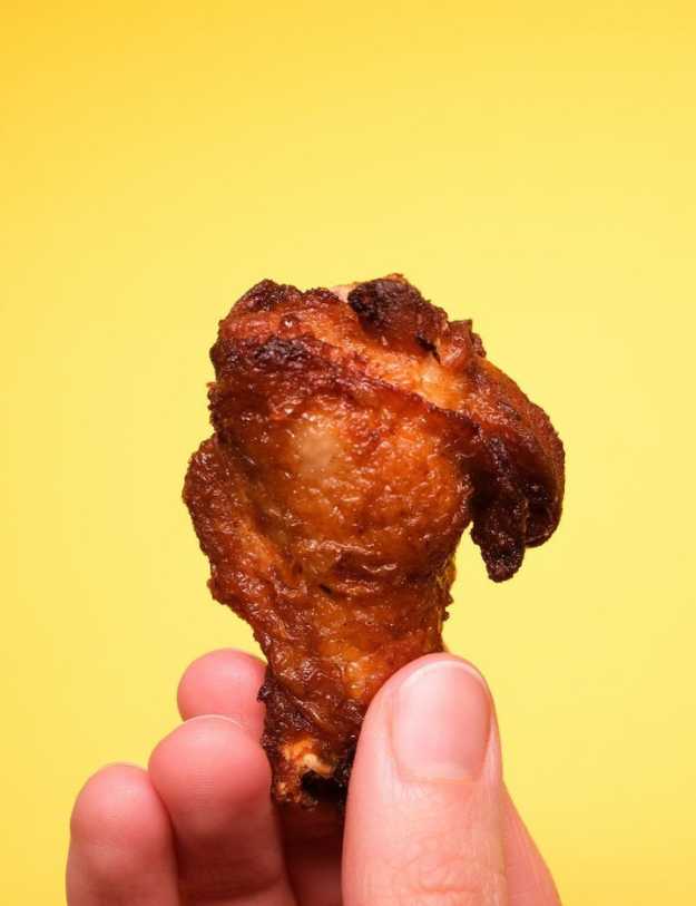Someone holding up a chicken leg in front of a yellow wall.