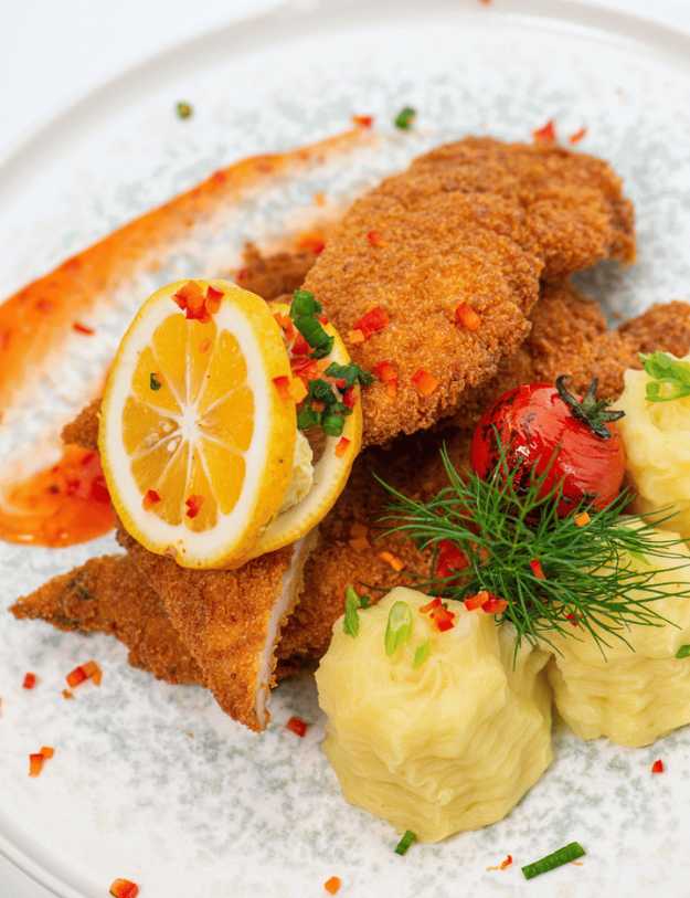 Deep fired fish with lemon and fruits placed onto a plate nicely.