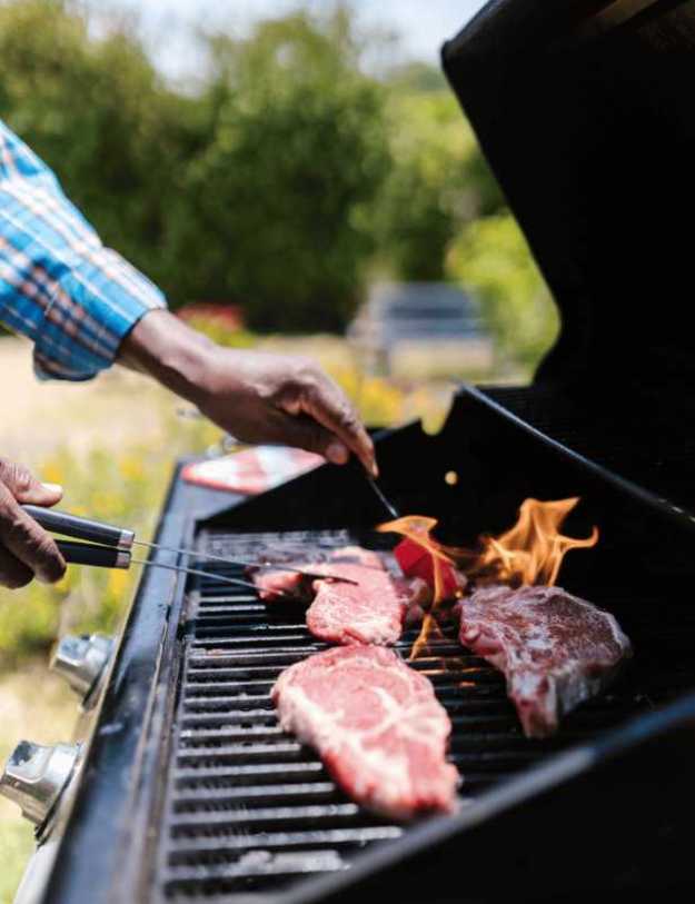 Colored person flipping steaks on a grill.